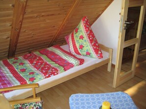 A small, single-bed room with a sloped ceiling and wooden walls.