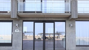 Entrada de edificio con puertas dobles, un balcón y la palabra 'VERBOETE' en las puertas de cristal.