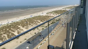 A beach view from a balcony with a clear sky, sandy beach, and a few people walking. - Apartment in Nieuwpoort With Ocean Views (Nieuwpoort)
