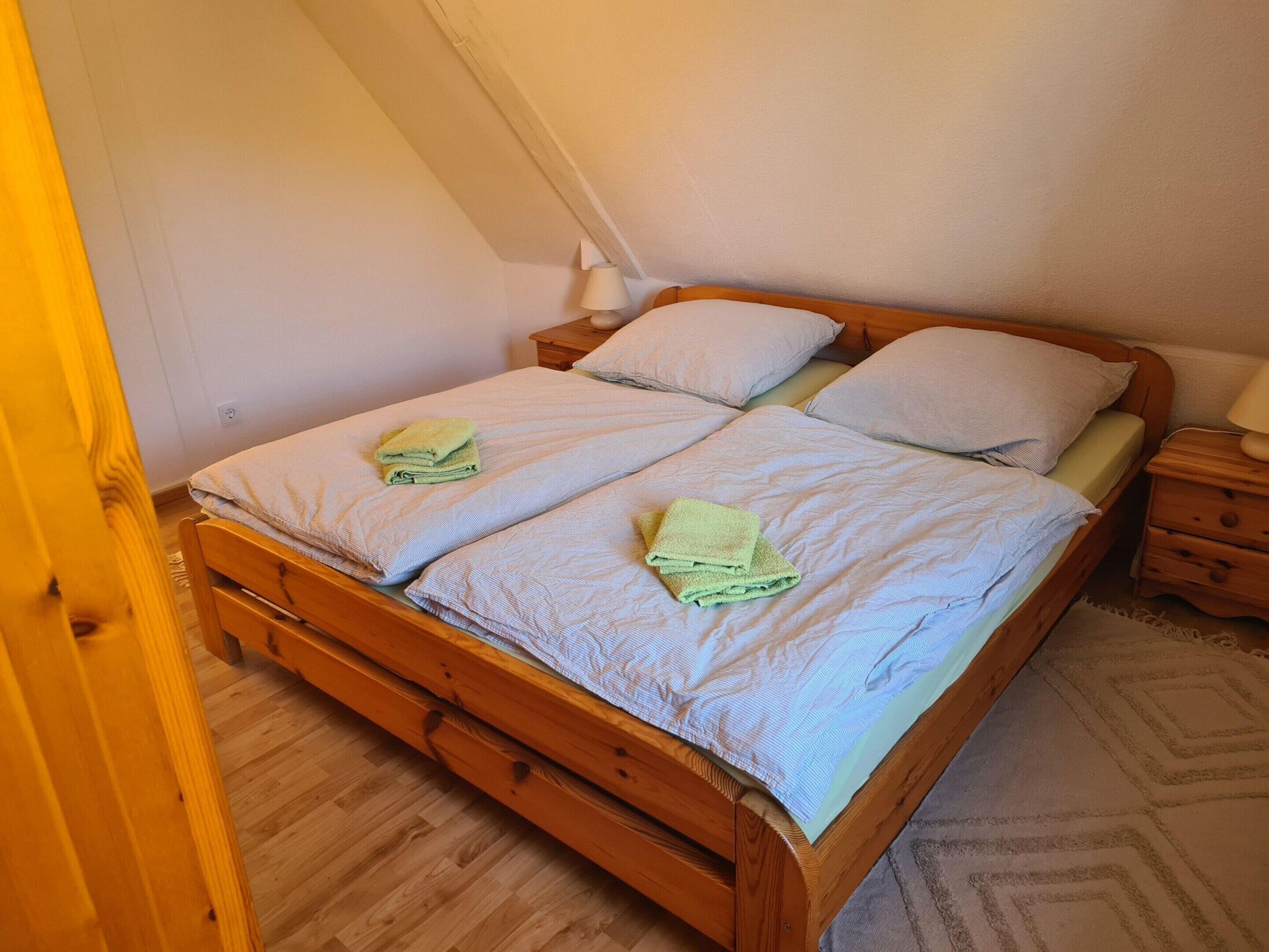 A wooden bed with two pillows and a folded towel on each side.