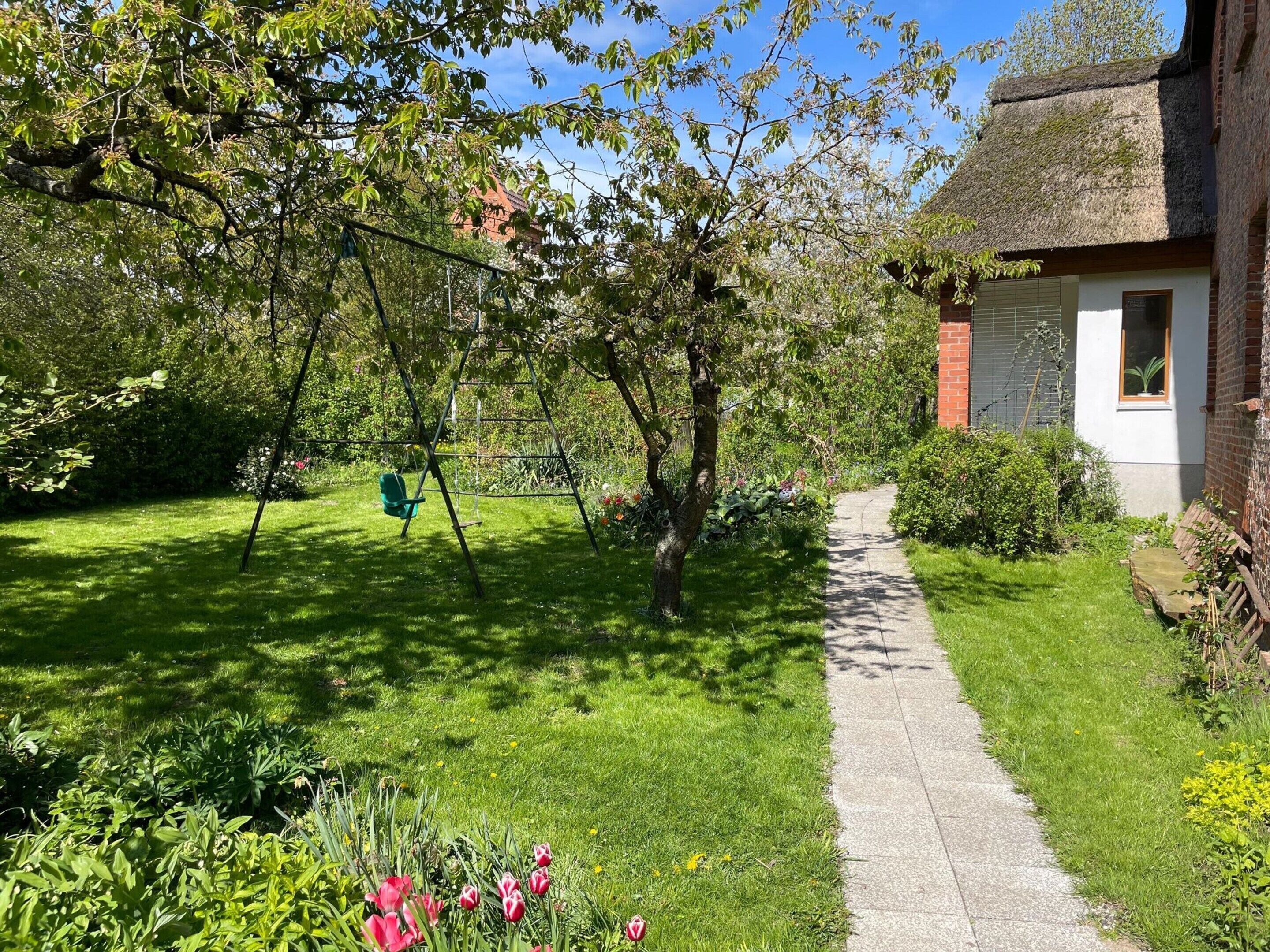 A garden with a swing set, a pathway, and a building with a thatched roof.