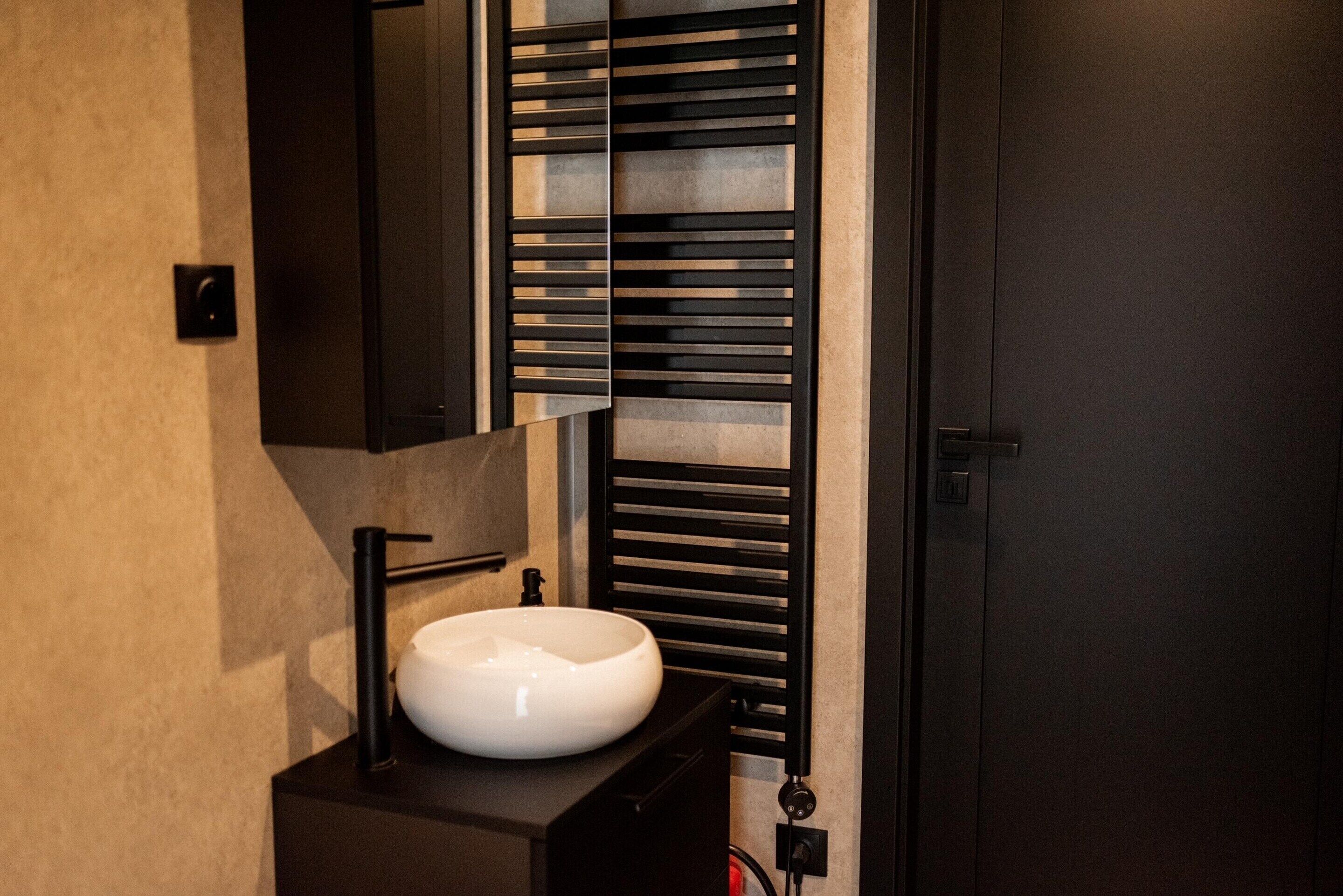 A modern bathroom with a white sink, black towel rack, and a mirror.