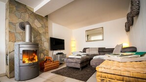 A cozy living room with a stone wall, a fireplace, a television, and comfortable seating. - Holiday Home Country House on Himmelsberg (Willebadessen)