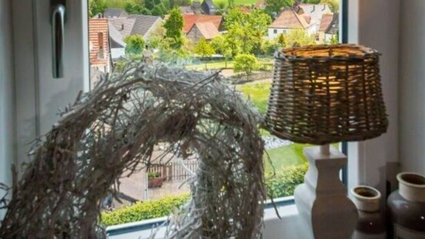 A room with a large window overlooking a rural landscape, a wicker lamp, and a decorative wreath. - Holiday Home Country House on Himmelsberg (Willebadessen)