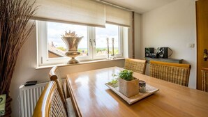A dining area with a wooden table, wicker chairs, a radiator, a window with a view, and a decorative vase. - Holiday Home Country House on Himmelsberg (Willebadessen)