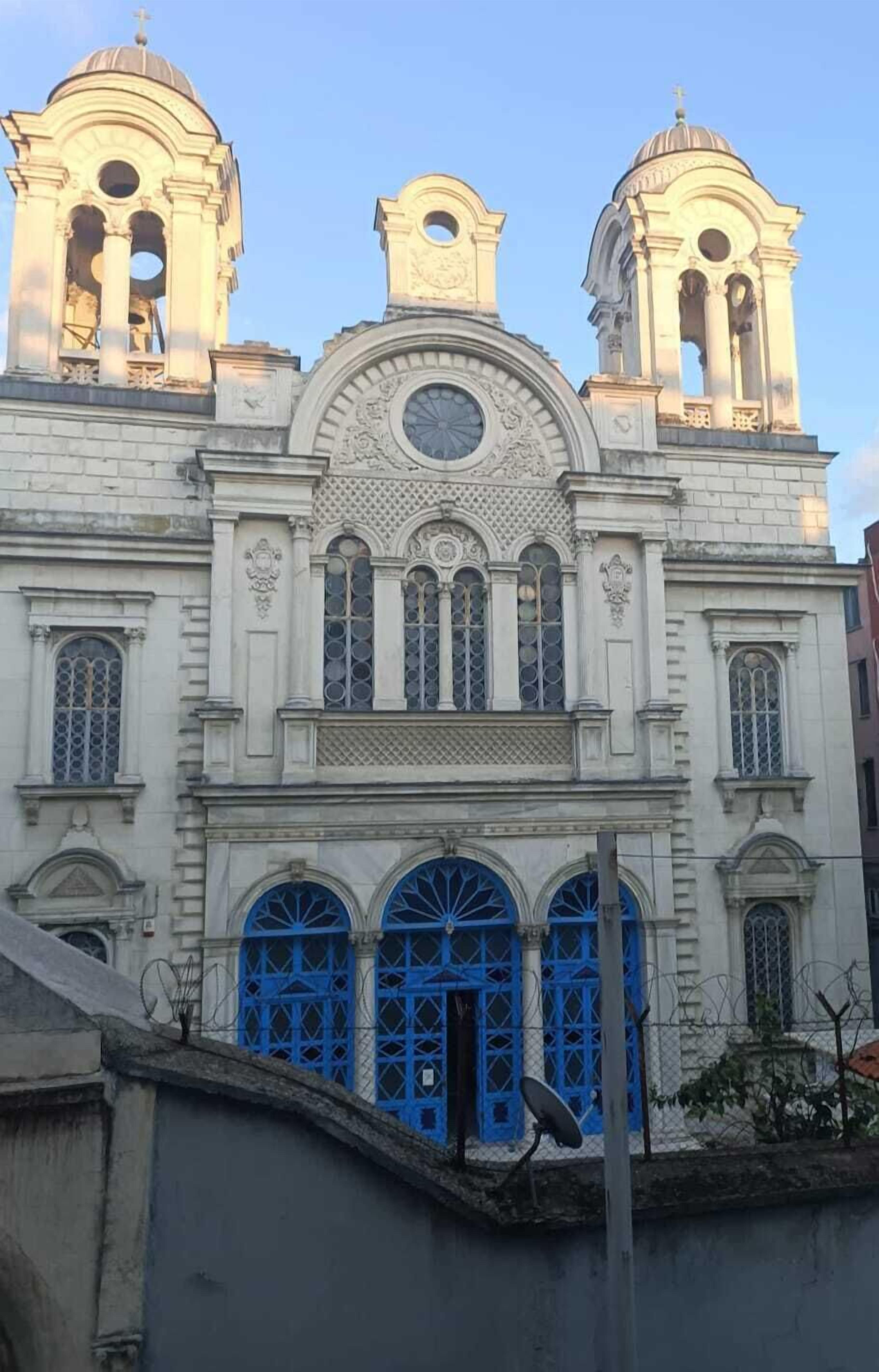 A historic building with a central dome, two bell towers, and blue doors.