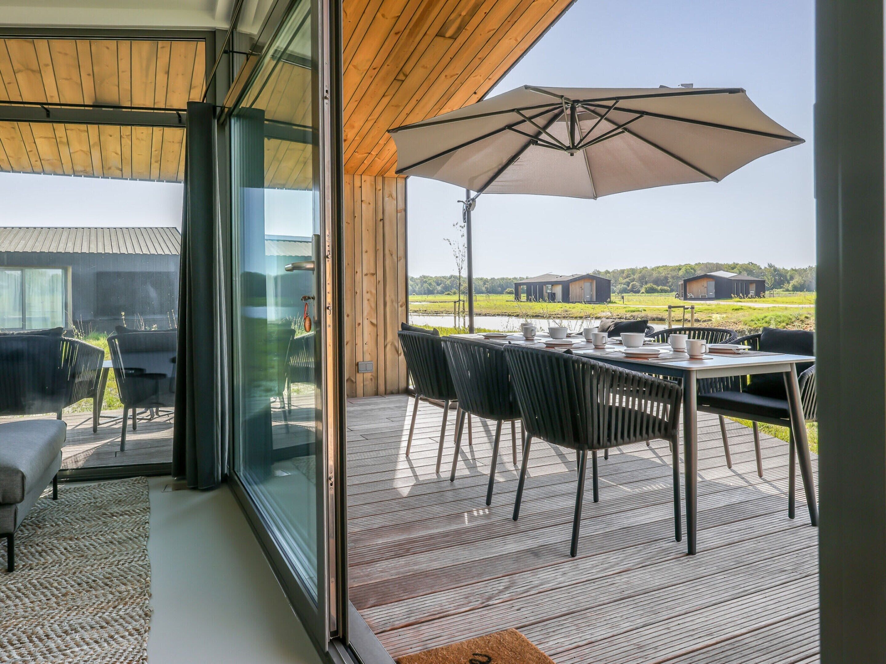 A modern outdoor dining area with a table and chairs, an umbrella, and a view of the countryside.