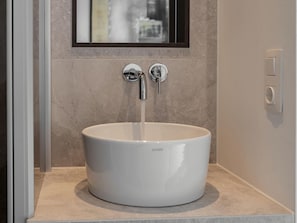 Un lavandino in ceramica bianca con un rubinetto singolo, posato su un piano di lavoro beige in un bagno.