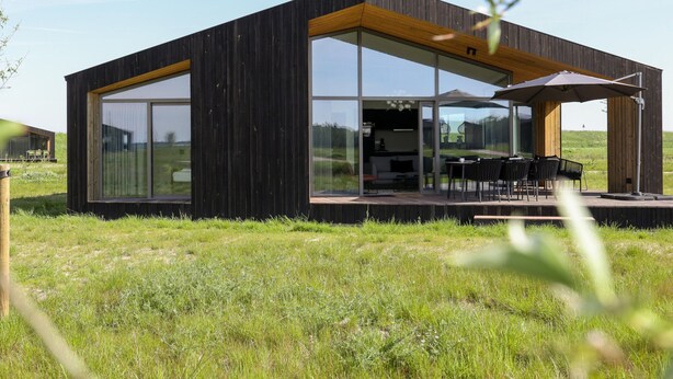 A modern, minimalist house with large glass windows, an outdoor dining area, and a wooden deck. - Cottage in Wissenkerke Near Nature Reserve (Wissenkerke)
