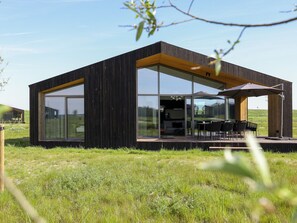 Una casa moderna y minimalista con amplios ventanales, un área de comedor exterior y una terraza de madera.
