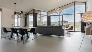 A modern interior with a dining area, sofa, and large windows offering a view of the outdoors. - Cottage in Wissenkerke Near Nature Reserve (Wissenkerke)