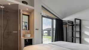 A modern bedroom with a large bed, a bathroom with a shower, and a view of the outdoors. - Cottage in Wissenkerke Near Nature Reserve (Wissenkerke)