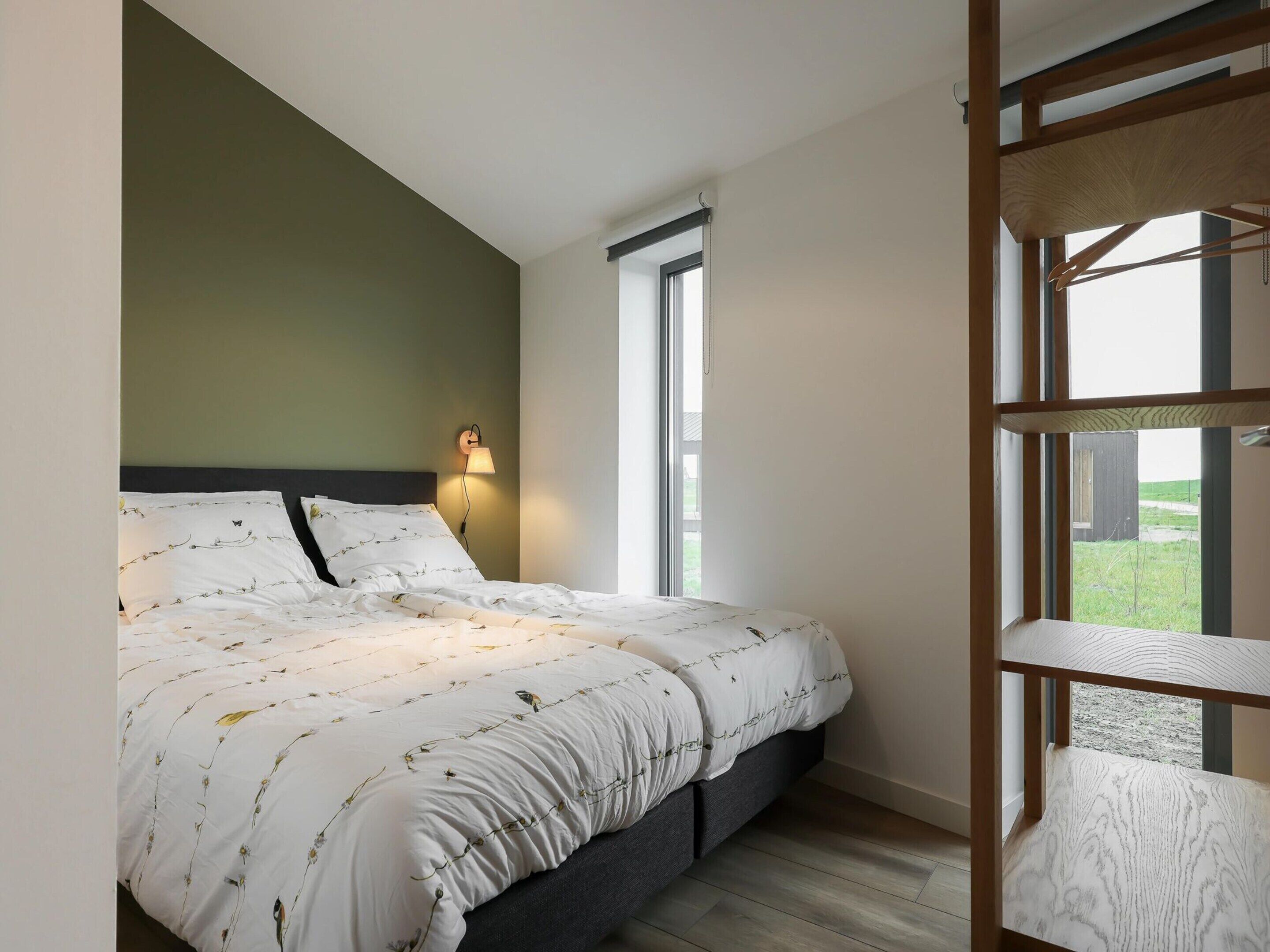 A bedroom with a bed, a nightstand, a wall-mounted lamp, and a window.