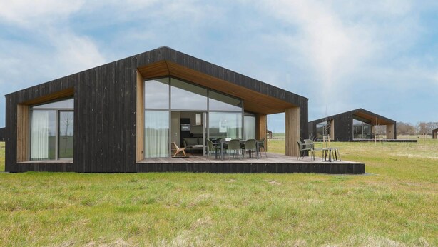 Una casa moderna y minimalista con amplios ventanales y techo plano, ubicada en un campo cubierto de hierba.