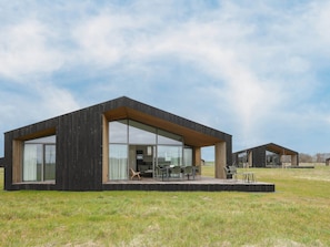 A modern, minimalist house with large glass windows and a flat roof, situated in a grassy field. - Cottage in Wissenkerke Near Het Bokkegat (Wissenkerke)