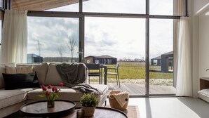 A modern living room with a sofa, two round tables, and a view of a grassy field through large windows. - Inviting Holiday Home in the Nature (Wissenkerke)