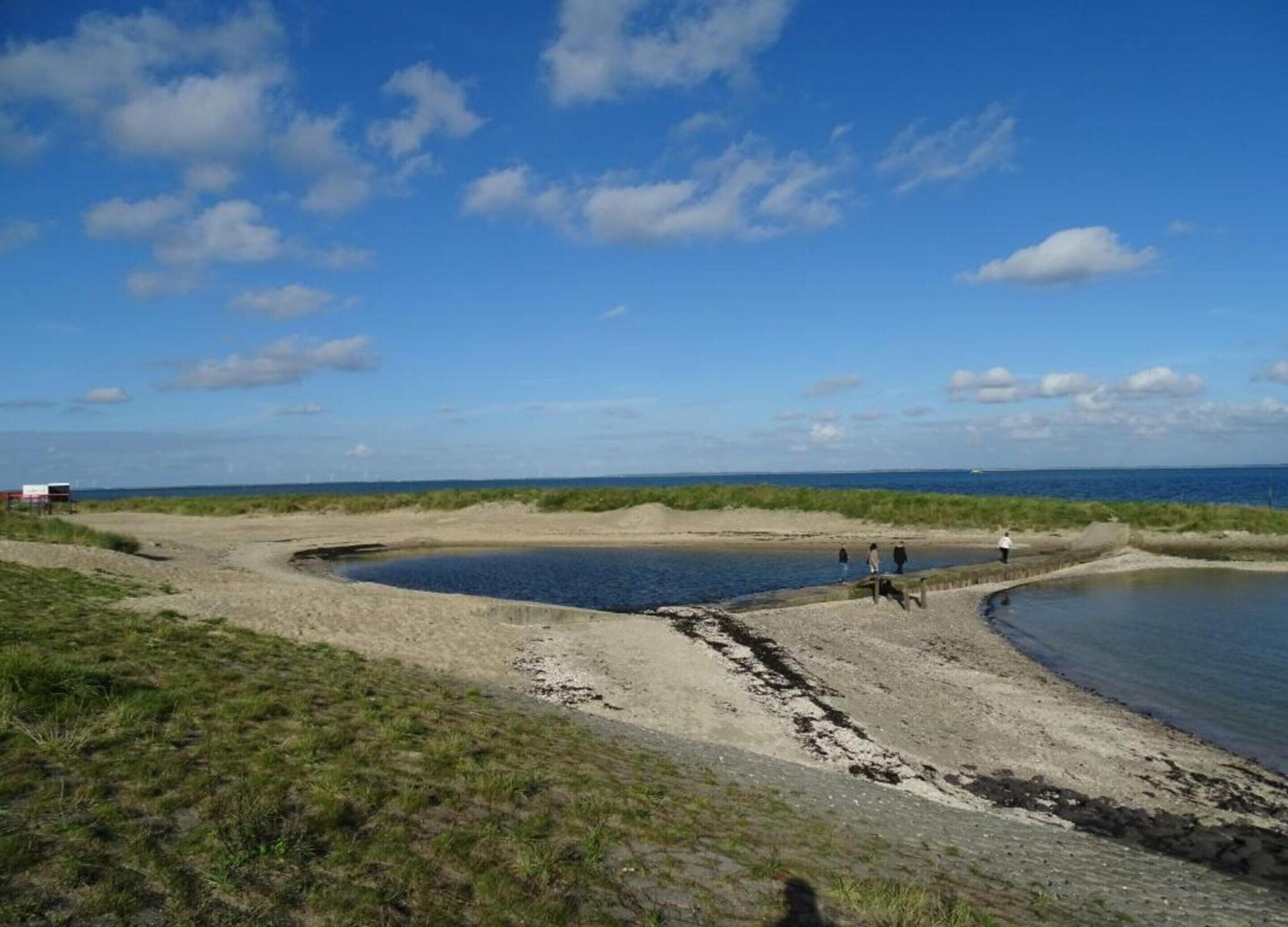 A coastal landscape with a sandy beach, a small water body, and grassy dunes.