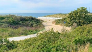 A coastal path leading to a beach with a white fence and dense greenery. - Scenic Cottage w/ Garden (Wissenkerke)