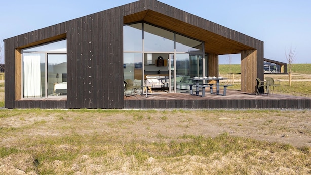 A modern wooden cabin with large glass windows, a patio with outdoor seating, and a view of the surrounding landscape. - Holiday Home Wissenkerke Near Nature Reserve (Wissenkerke)