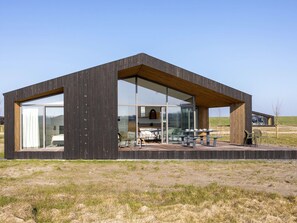Une cabane moderne en bois, dotée de grandes fenêtres en verre, d’une terrasse avec des meubles d’extérieur et offrant une vue sur le paysage environnant.