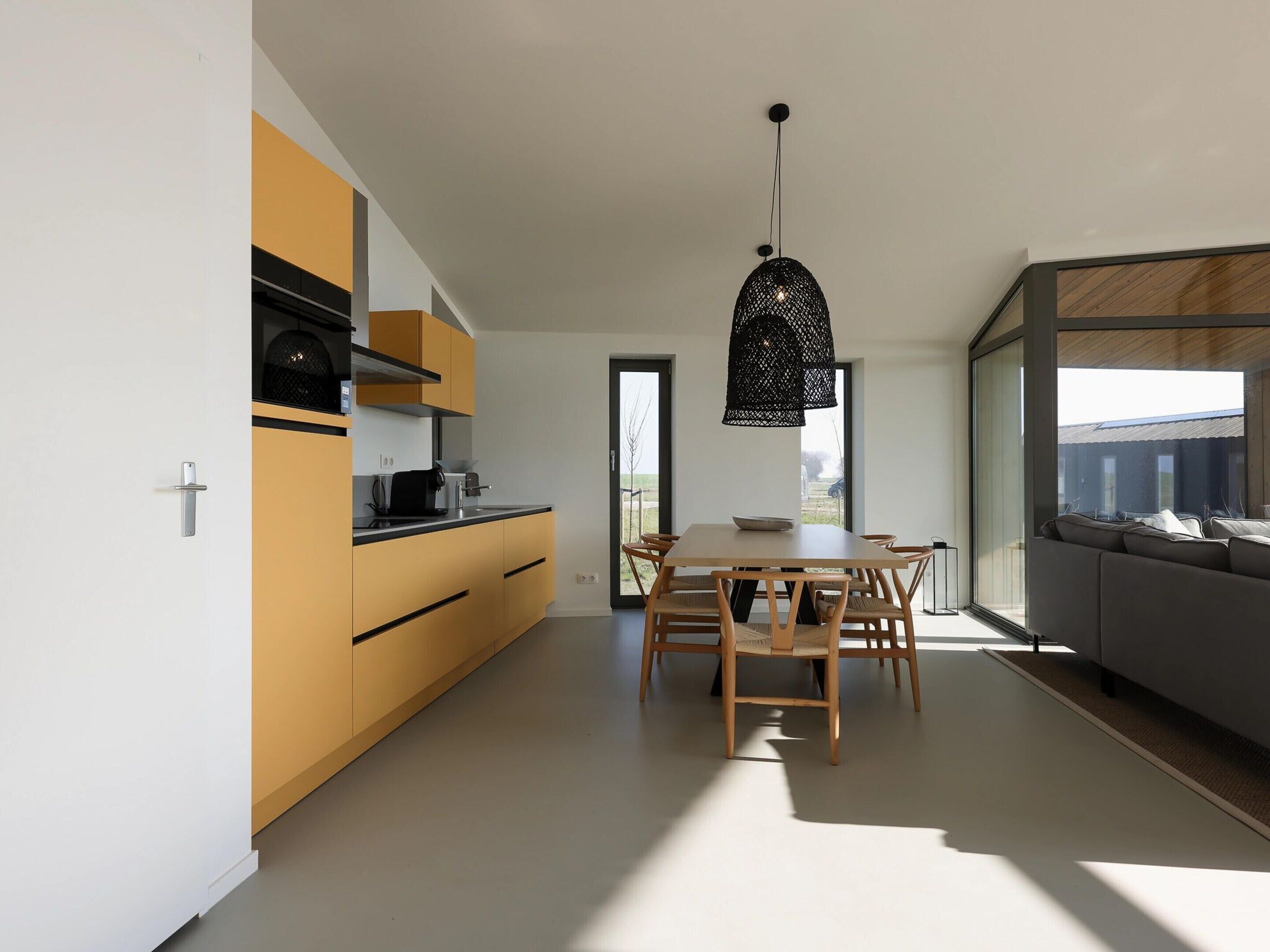 A modern kitchen with a dining area, featuring a large window, a black hanging light fixture, and a built-in oven.