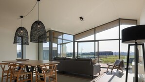 A modern living room with a large window, a wooden dining table, and a sofa. - Holiday Home Wissenkerke Near Nature Reserve (Wissenkerke)