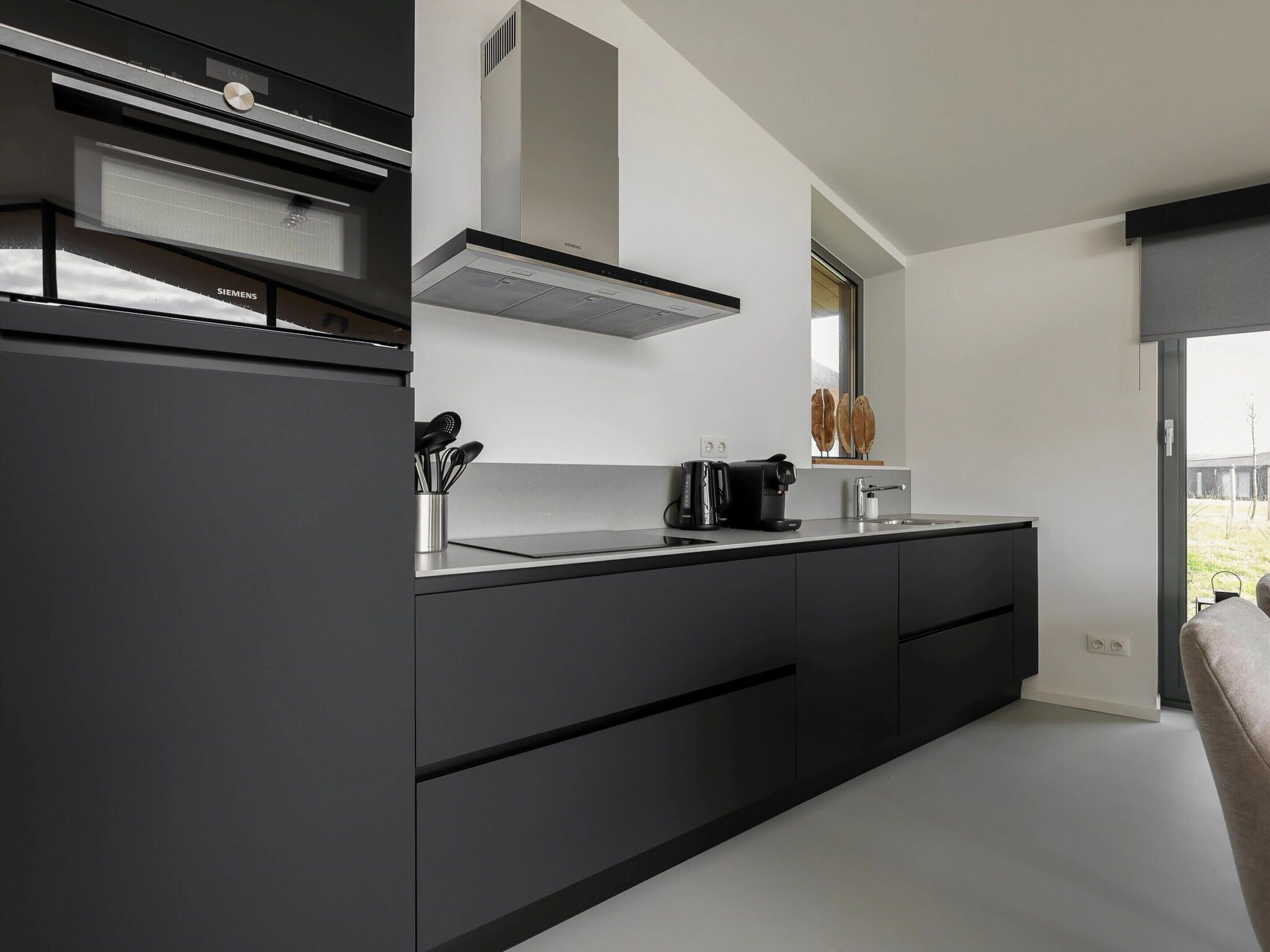 Una cocina moderna con encimera negra, extractor Siemens y ventana con vistas al exterior.