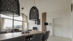 A modern dining area with a wooden table, grey upholstered chairs, and black pendant lights. - Holiday Home Wissenkerke Near Nature Reserve (Wissenkerke)