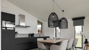 A modern kitchen with a central island, black pendant lighting, and a dining area with grey chairs and a wooden table. - Holiday Home Wissenkerke Near Nature Reserve (Wissenkerke)