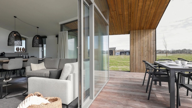 A modern living space with a sofa, dining table, and chairs. There is a kitchen area with a counter and cabinets. The room has large windows and a view of the outdoors. - Holiday Home Wissenkerke Near Nature Reserve (Wissenkerke)
