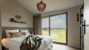 Un dormitorio con una cama grande, una lámpara colgante, una ventana con vistas al exterior y un estante con adornos.