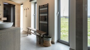 Un baño moderno con un lavamanos grande, un banco, toallero y vistas a través de una puerta de cristal.