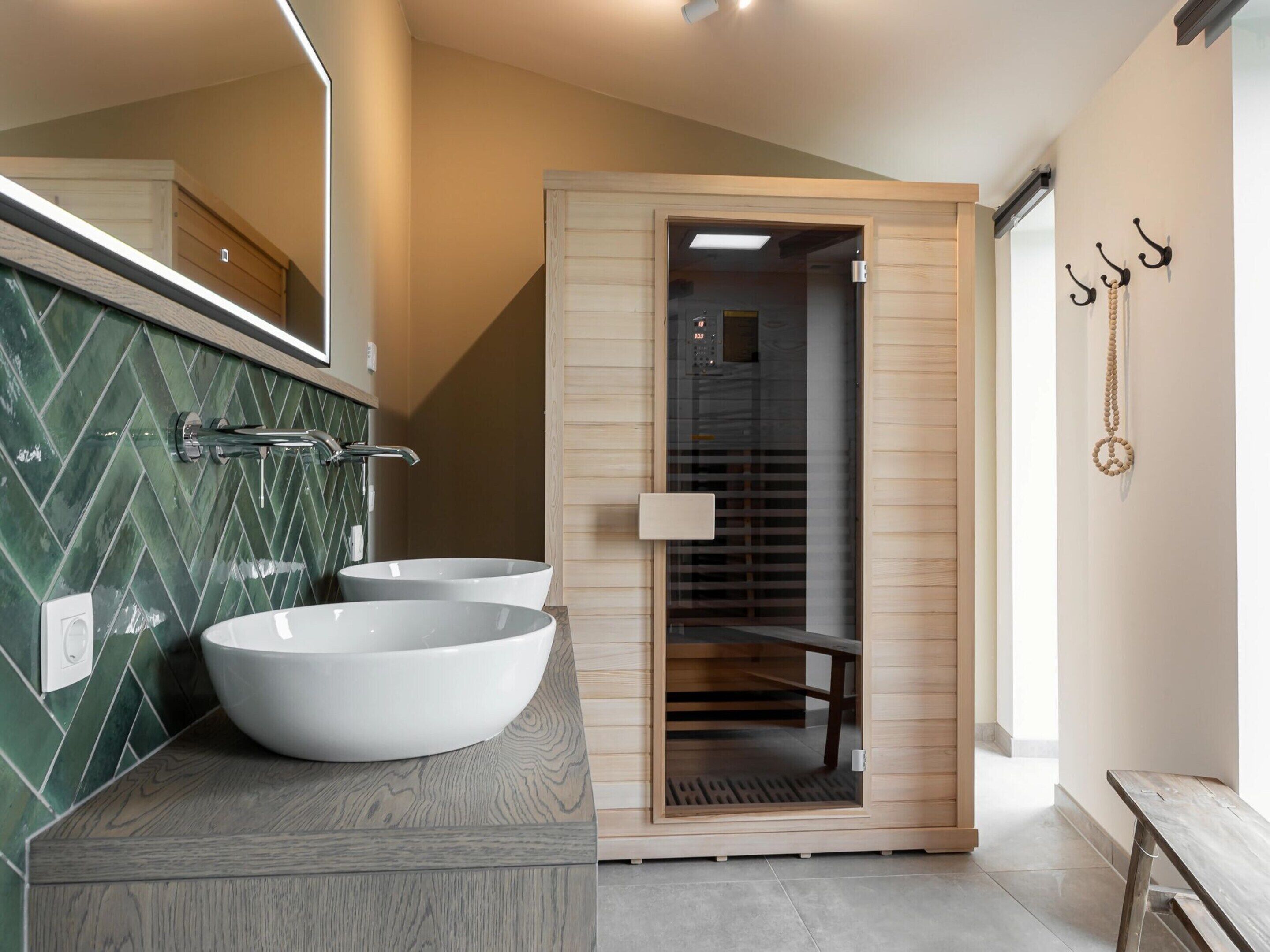 A modern bathroom with two large white sinks, a wooden vanity, a mirror, and a walk-in shower with a glass door.