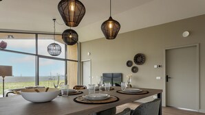 Un comedor moderno con una mesa larga, dos lámparas colgantes y vistas al exterior.