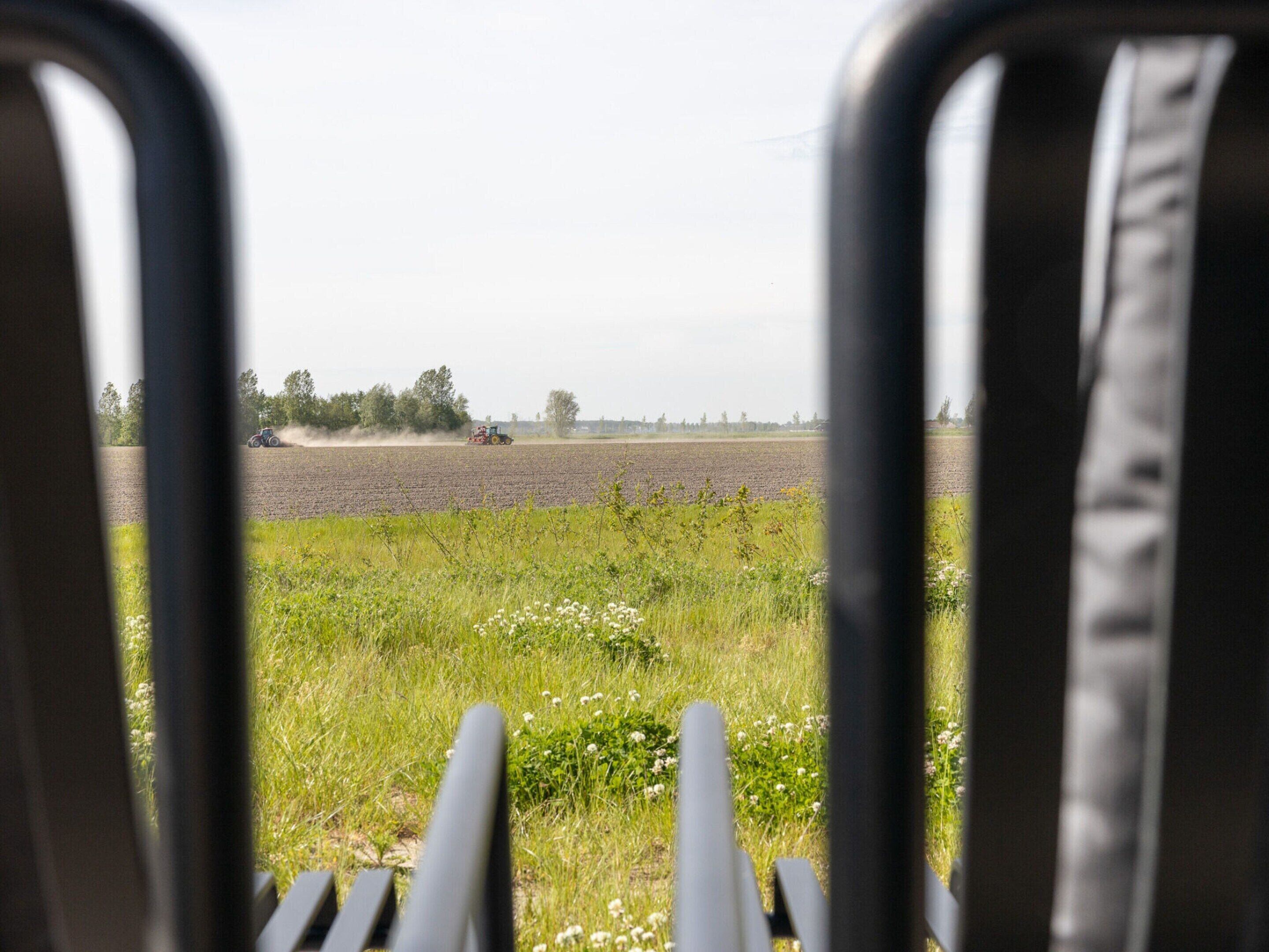 A view through a window with a metal frame, looking out at a field with a tractor in the distance.