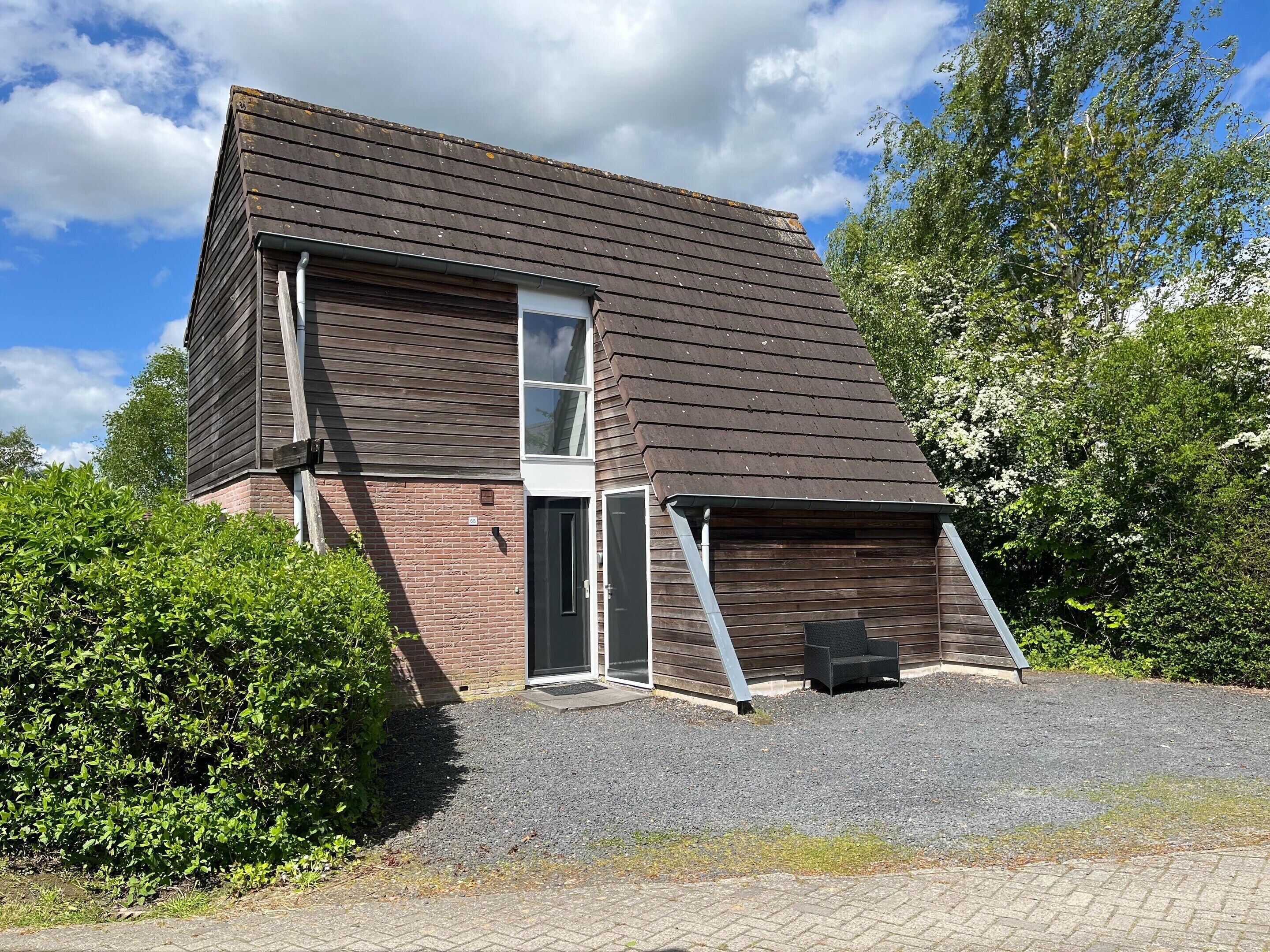 Een huis met twee verdiepingen, een schuin dak, een bakstenen gevel en een grindpad.