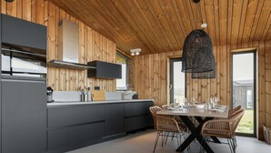 A modern kitchen with wooden paneling, a dining area with wicker chairs, and a large window. - Cottage in Wissenkerke Near Nature Reserve (Wissenkerke)