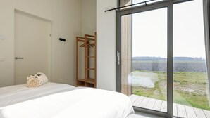 A bedroom with a bed, a wooden wardrobe, and a sliding glass door leading to a view of a field. - Cottage in Wissenkerke Near Nature Reserve (Wissenkerke)