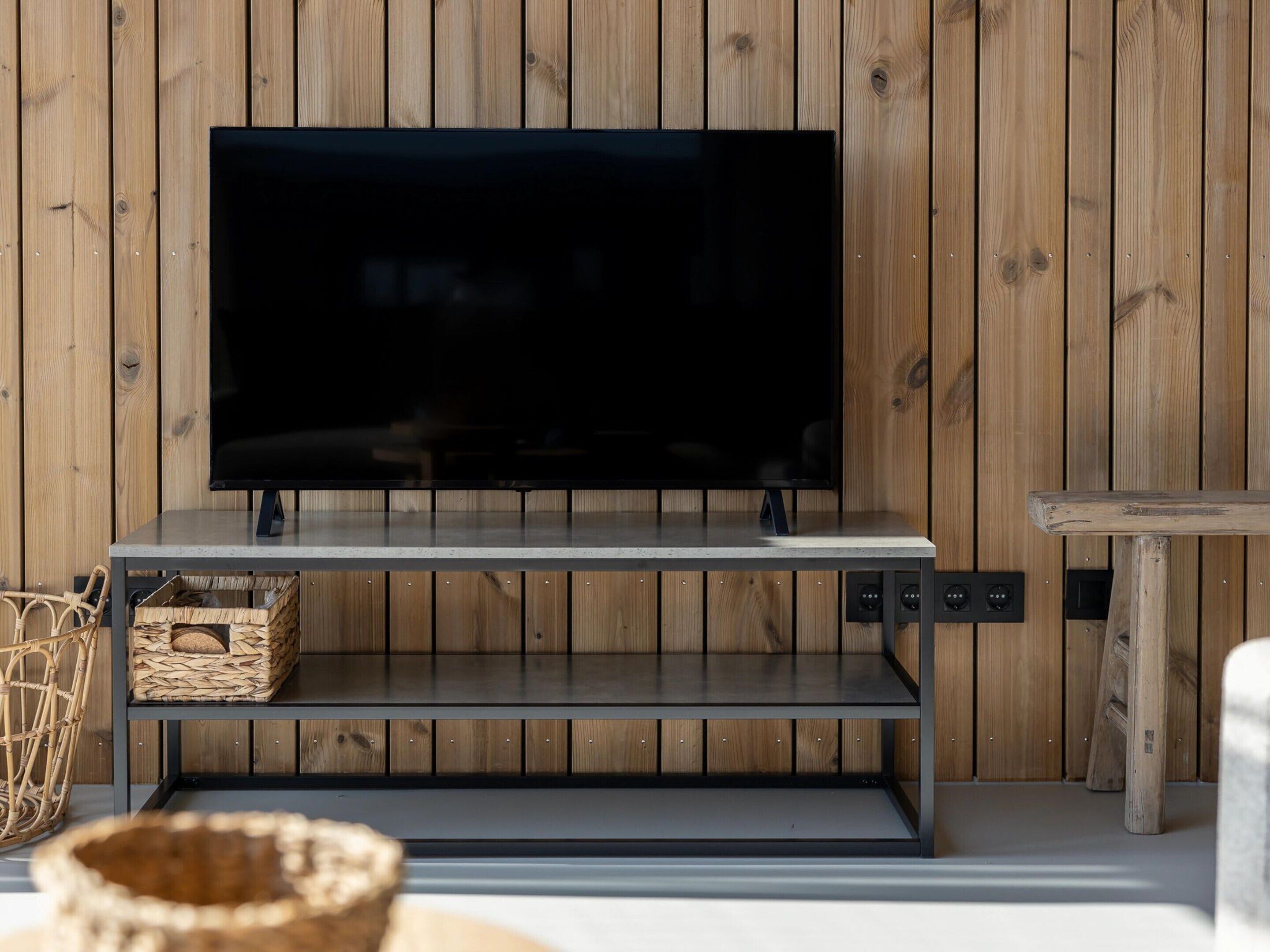 A flat-screen TV on a metal stand against a wooden wall.