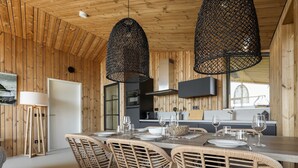 A modern kitchen with wooden walls, a dining table set for four, and two hanging pendant lights. - Cottage in Wissenkerke Near Nature Reserve (Wissenkerke)