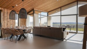 A modern interior with a wooden ceiling, large windows, a dining area with wicker chairs, and a sofa. - Cottage in Wissenkerke Near Nature Reserve (Wissenkerke)