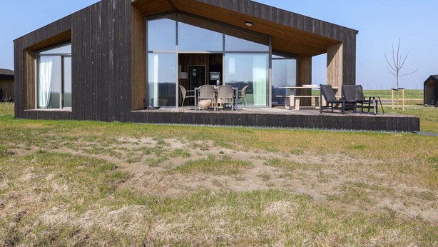 A modern wooden house with large glass windows, a deck with outdoor furniture, and a clear view of the surrounding landscape. - Cottage in Wissenkerke Near Nature Reserve (Wissenkerke)