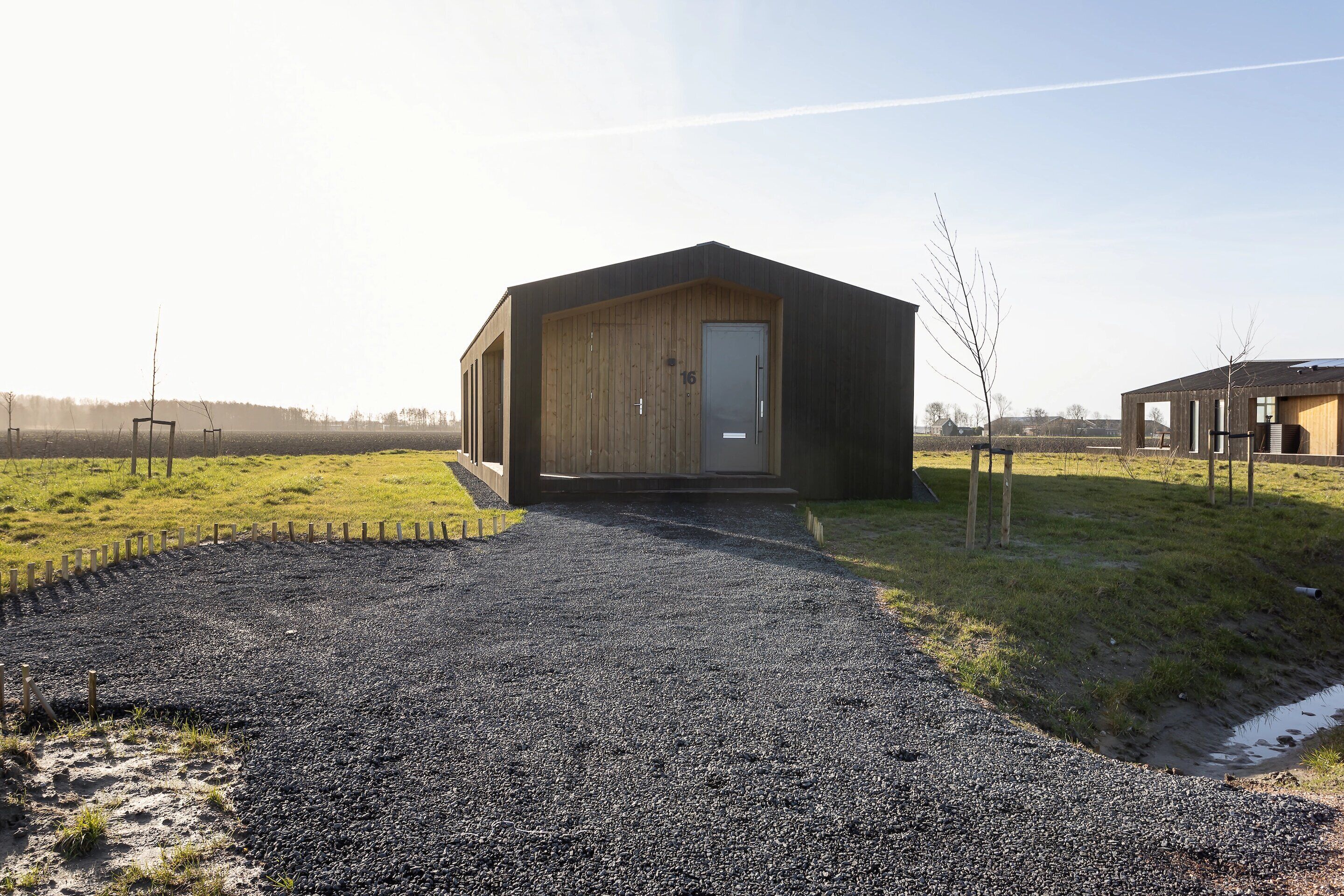 A modern building with a wooden door and a gravel driveway leading to it.