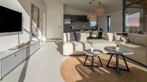 Un salon moderne doté d’un grand téléviseur à écran plat, d’un canapé, d’une table basse et d’un coin repas avec une cuisine en arrière-plan.