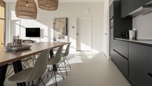 Une cuisine moderne avec des meubles de couleur sombre, une table à manger en bois et trois suspensions en osier.