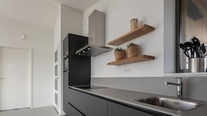 A modern kitchen with grey cabinets, a stainless steel sink, and wooden shelves with plants. - Cottage in Wissenkerke Near Het Bokkegat (Wissenkerke)