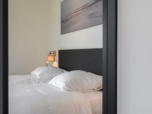 A neatly made bed with white linens and pillows, a dark headboard, and a wall-mounted lamp. - Cottage in Wissenkerke Near Het Bokkegat (Wissenkerke)