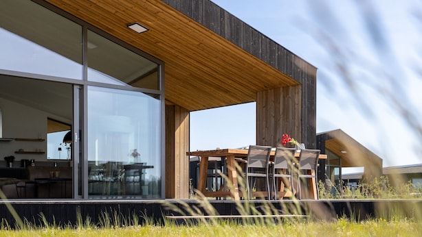 A modern house with large glass windows, a wooden deck, and a dining area with outdoor furniture. - Cottage in Wissenkerke Near Het Bokkegat (Wissenkerke)