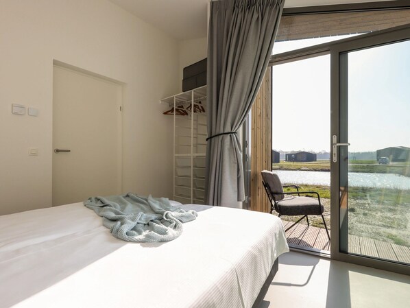 Une chambre à coucher comprenant un lit, un placard et donnant sur un plan d’eau et un paysage.