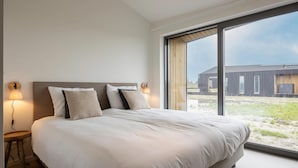 A bedroom with a large bed, two bedside lamps, and a view of the outside through a large window. - Lovely Holiday Home in Wissenkerke With Garden (Wissenkerke)